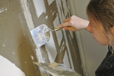 Ein Arbeiter mit Handschuhen verteilt während Reparaturarbeiten mit einer Kelle weissen Gips an einer Wand.