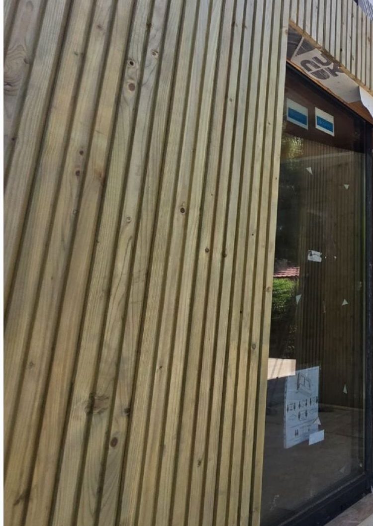 Bardage extérieur en lattes de bois, incliné, sur un bâtiment. Fenêtre visible à droite.