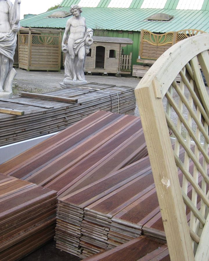Des piles de planches de bois brun et des objets décoratifs de jardin sont exposés.