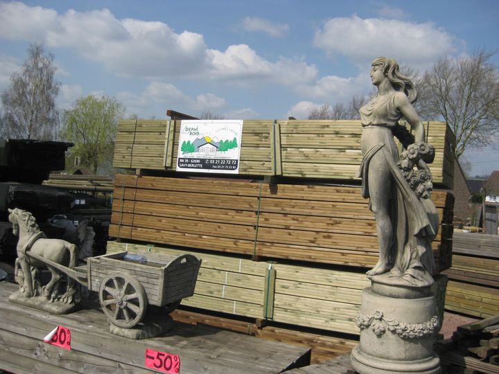 Une scène de scierie avec du bois empilé, une statue classique et des statues de charrettes tirées par des chevaux.
