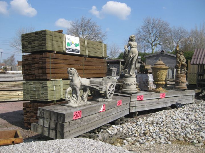 Sculptures en bois et en pierre à vendre dans un magasin d'articles de plein air. On y trouve notamment une charrette tirée par un cheval et une femme assise.