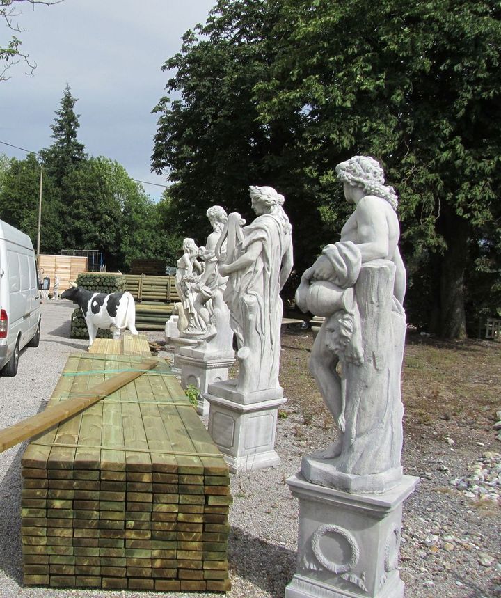Des statues sur des piédestaux, des piles de bois et une statue de vache tachetée dans un cadre extérieur.