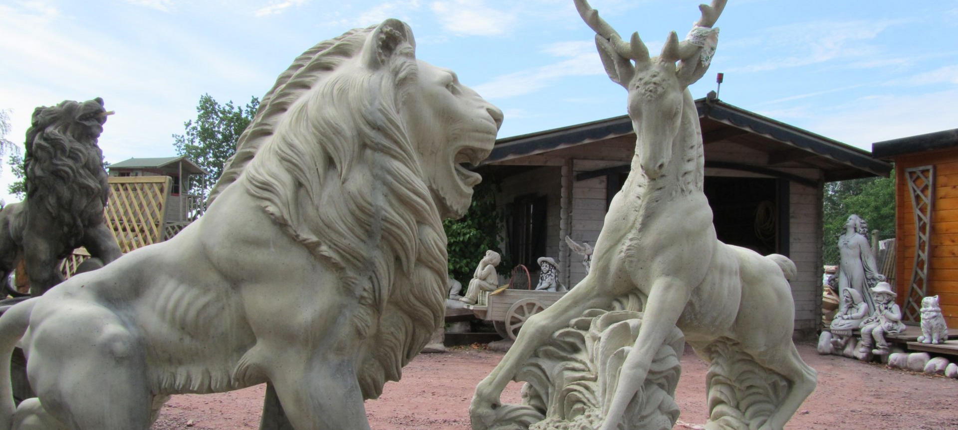 Statues de lion et de cerf en pierre dans un cadre extérieur. Lion rugissant, cerf aux grands bois. Bâtiments en arrière-plan.