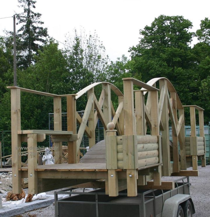 Structure de pont en bois sur remorque, prête à être installée, avec une conception arquée et une rambarde.