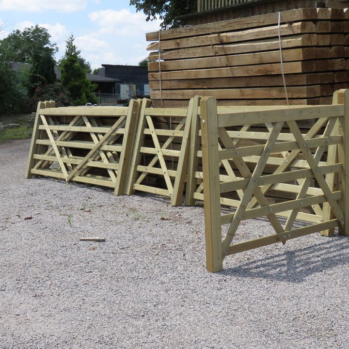 Trois portails de ferme en bois sur du gravier, avec du bois empilé en arrière-plan.