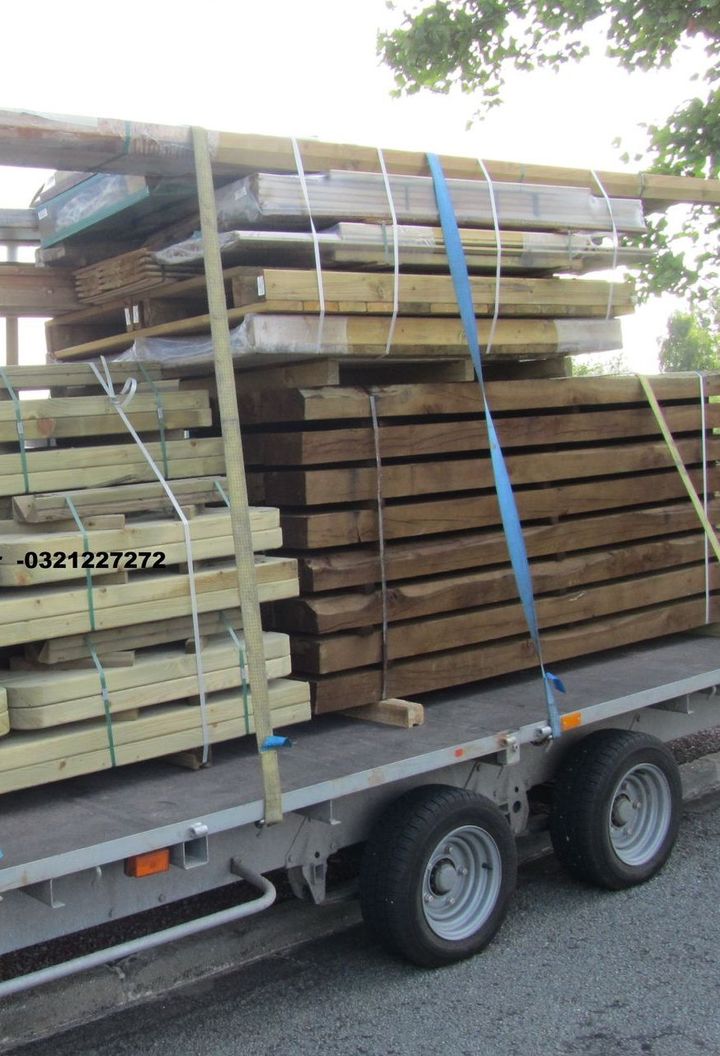 Des planches de bois fixées sur une remorque à l'aide de sangles bleues.