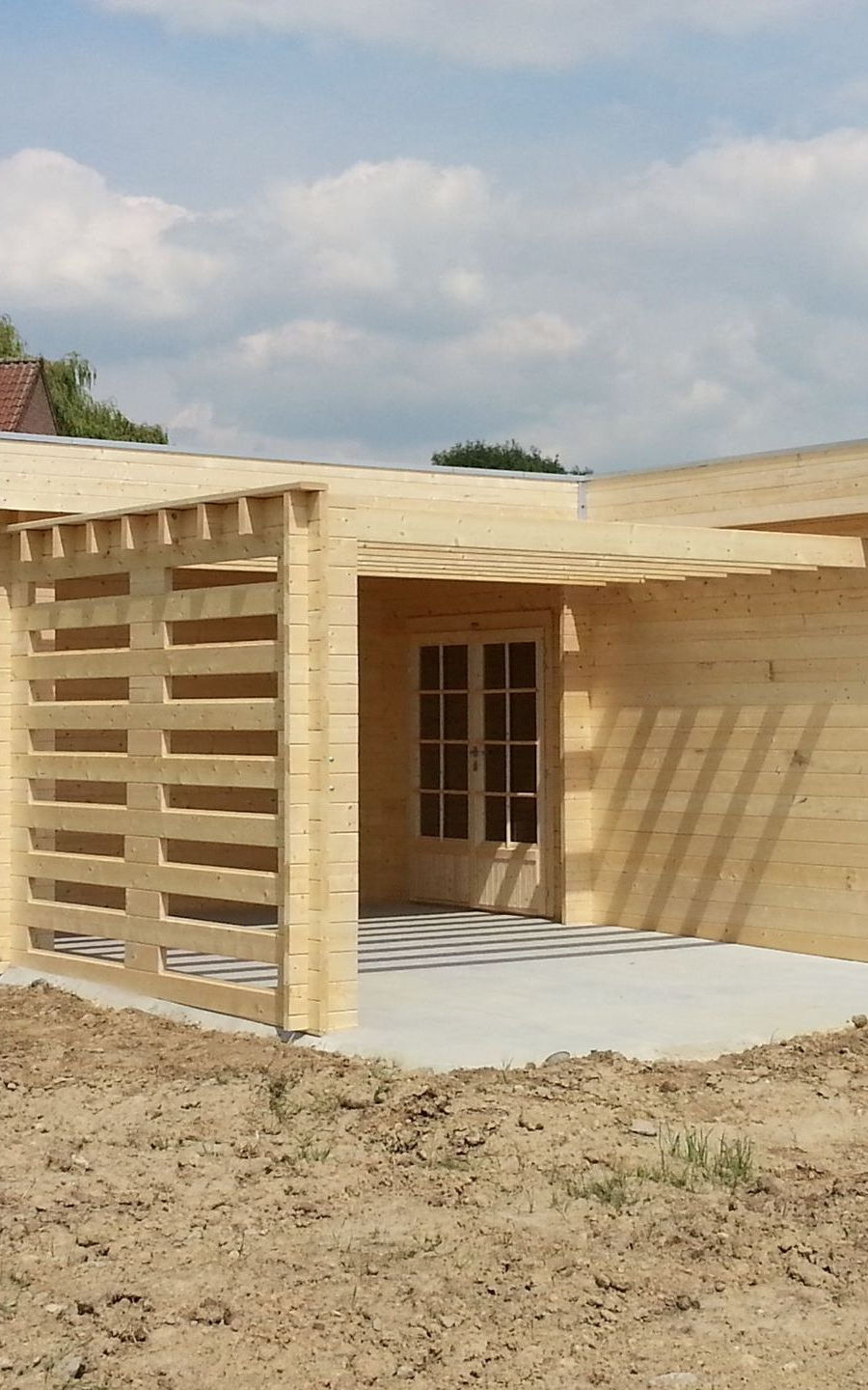 Cabane en bois avec véranda couverte en construction sur un terrain vague, sous un ciel nuageux.