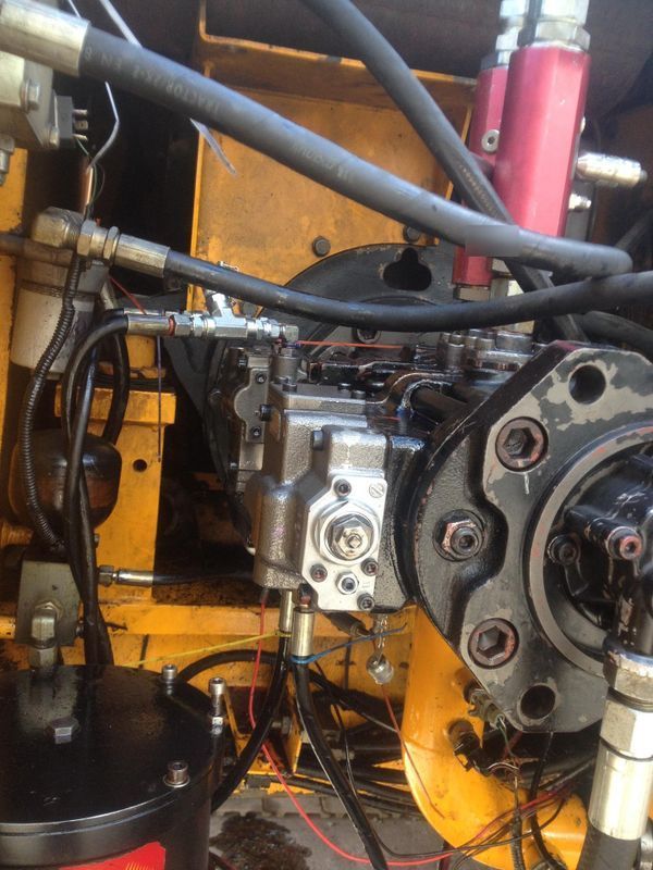 Gros plan sur une machinerie hydraulique avec des tuyaux, des raccords métalliques et un carter de moteur jaune à l'intérieur d'un atelier.