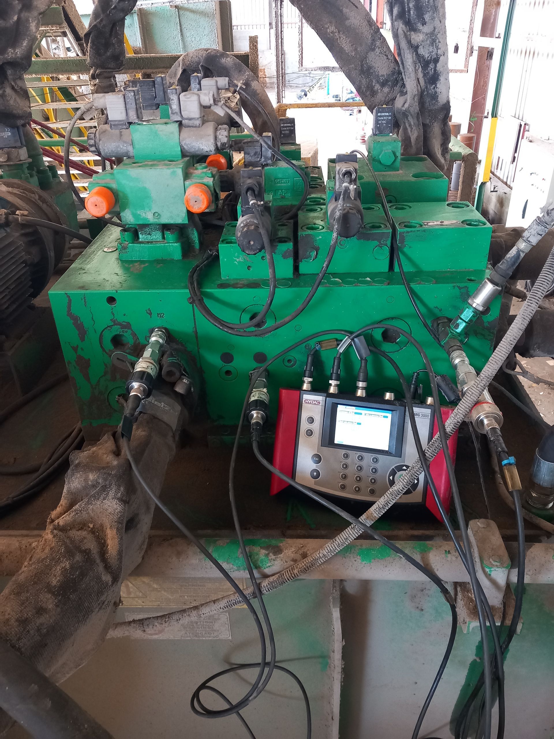 Machine industrielle verte dans un atelier, avec tuyaux, manomètres et panneau de commande sur une table.