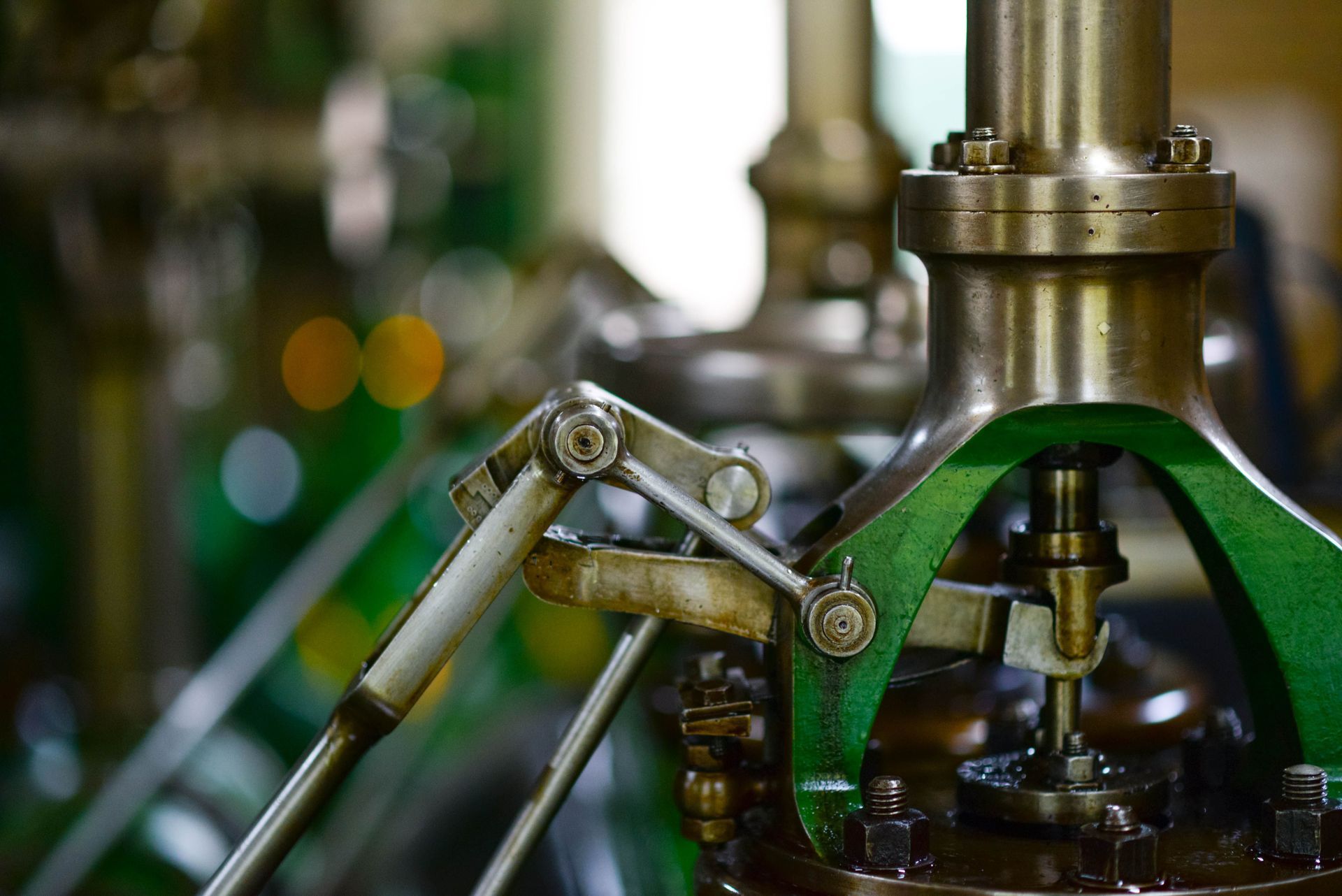 Gros plan sur une machine industrielle verte et en laiton, avec des articulations métalliques et un arrière-plan flou.