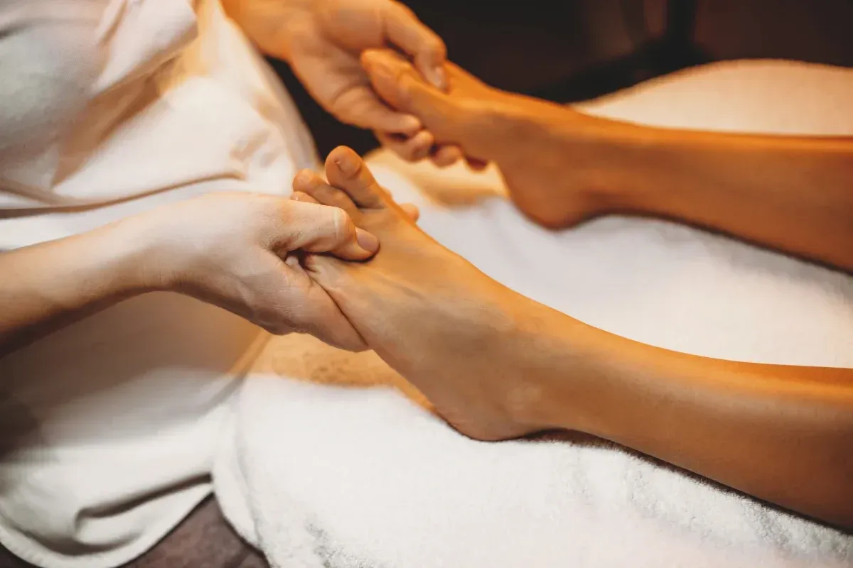 Manos masajeando un pie sobre una toalla blanca, probablemente en un spa.