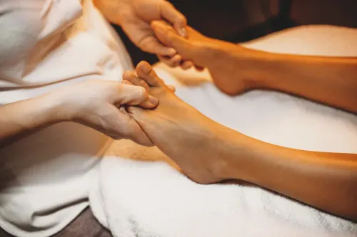 Manos masajeando un pie sobre una toalla blanca, probablemente en un spa.