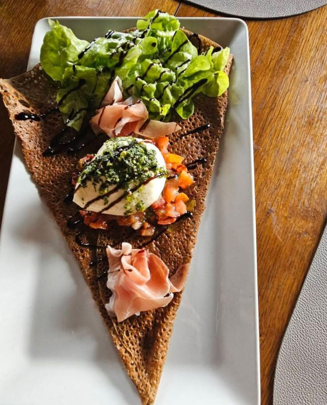 Part de galette servie avec de la crème, du jambon cru et de la salade