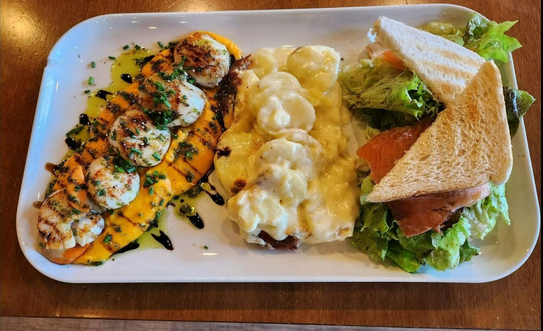 Noix de Saint-Jacques poêlées, servies avec une purée de légumes, un gratin de pomme de terre et une salade fraîche