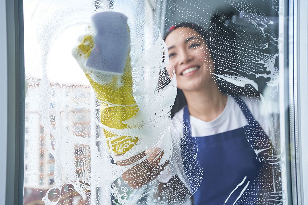 Eine Frau putzt lächelnd ein Fenster mit einem Schwamm.