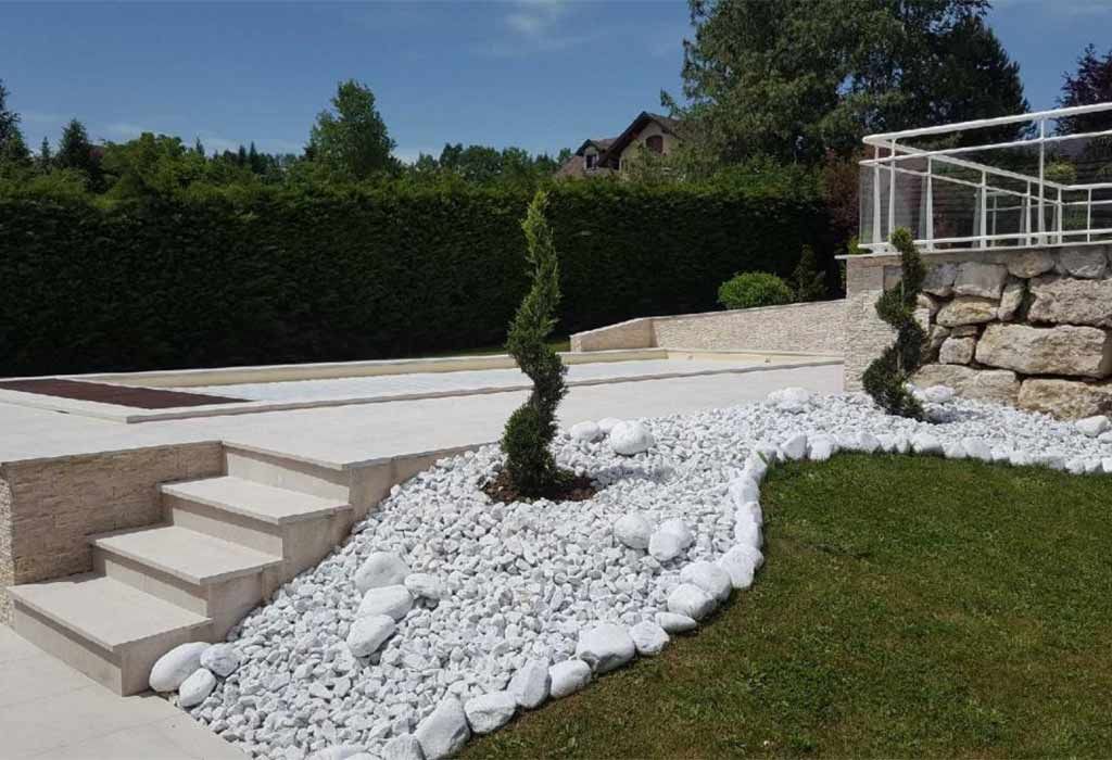 Terrasse de piscine avec escalier extérieur, deux arbustes taillés et des pierres blanches