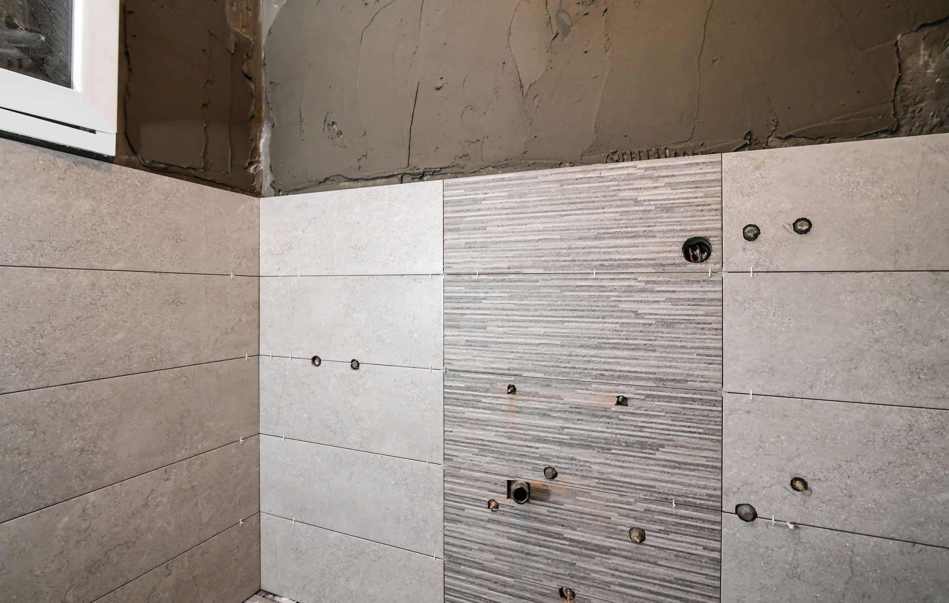 Pared del baño con azulejos sin terminar. Azulejos grises instalados en una pared gris.