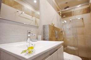 Baño con lavabo blanco, ducha con mampara de cristal e inodoro. Paredes beige claro.