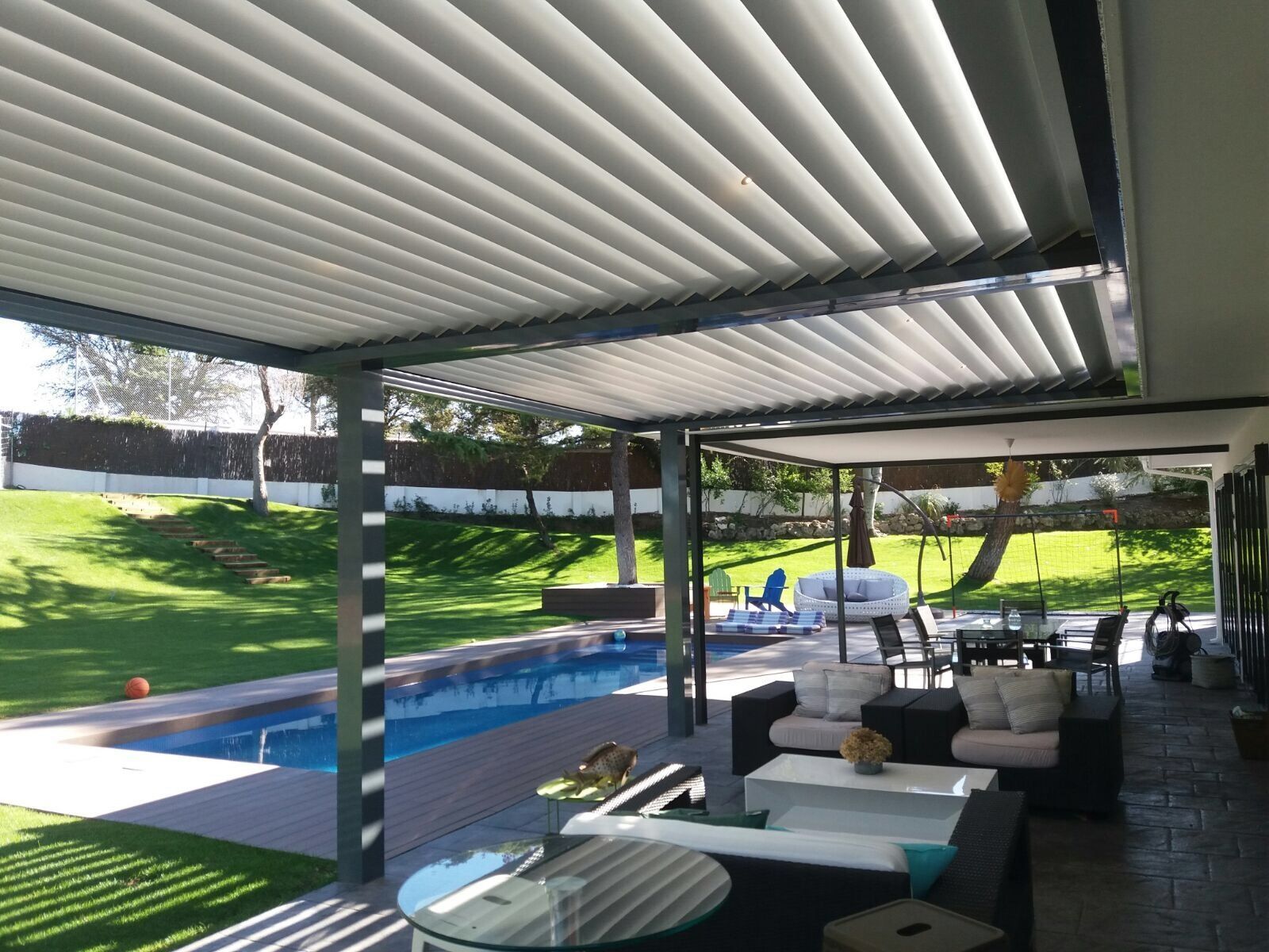 Un patio con pérgola y una piscina al fondo.