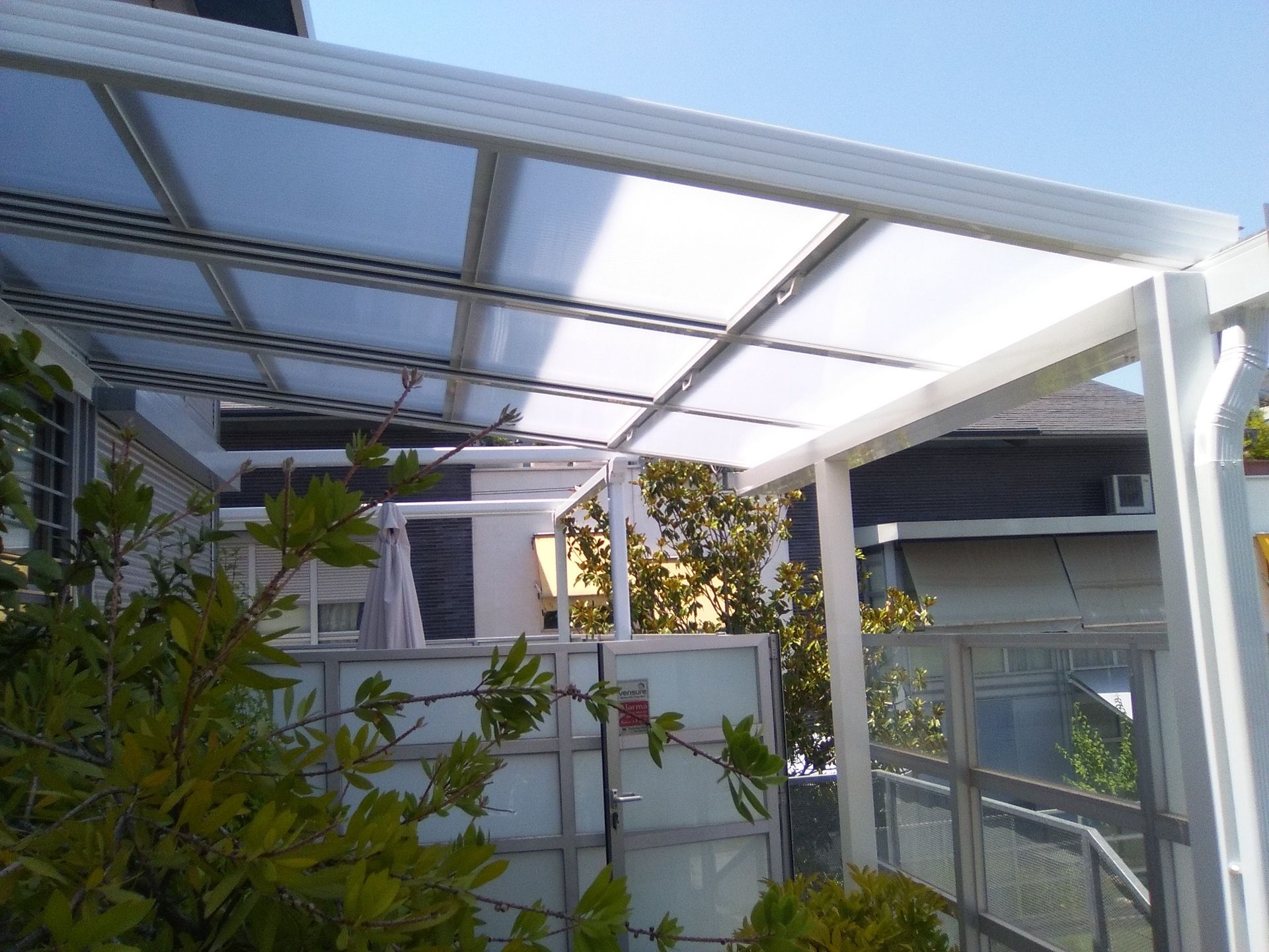 Una pérgola blanca con techo transparente está rodeada de árboles.