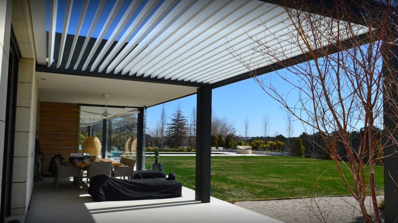 Un patio con una pérgola encima y un césped al fondo.
