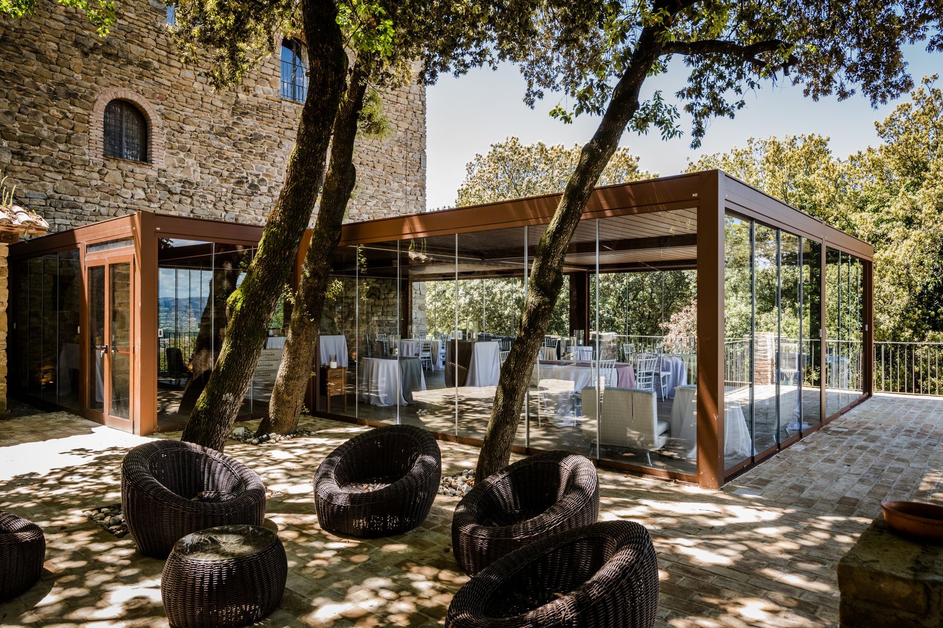 Un grupo de sillas están colocadas bajo una pérgola frente a un edificio de piedra.