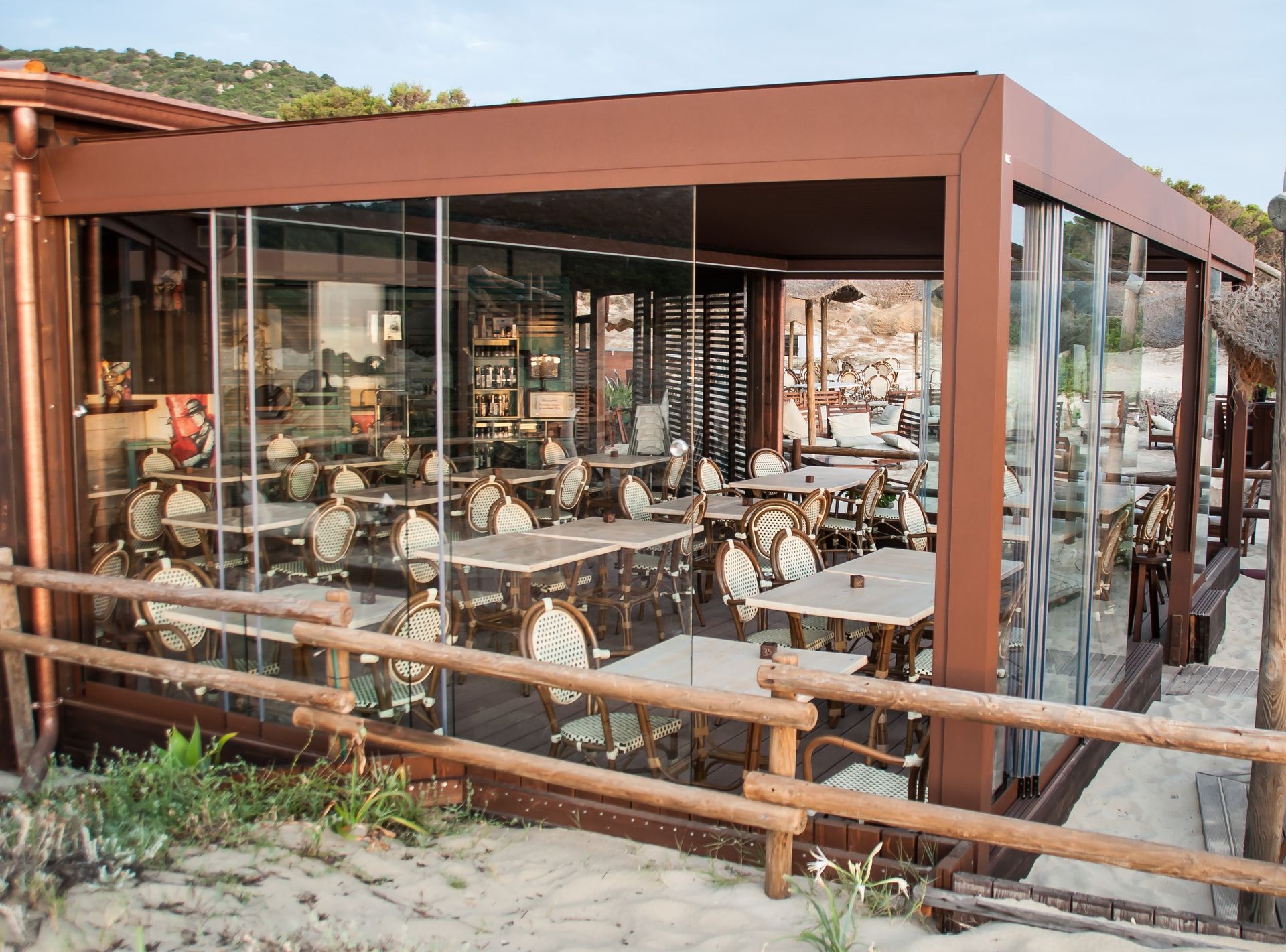 Un restaurante con mesas y sillas bajo una pérgola en la playa.
