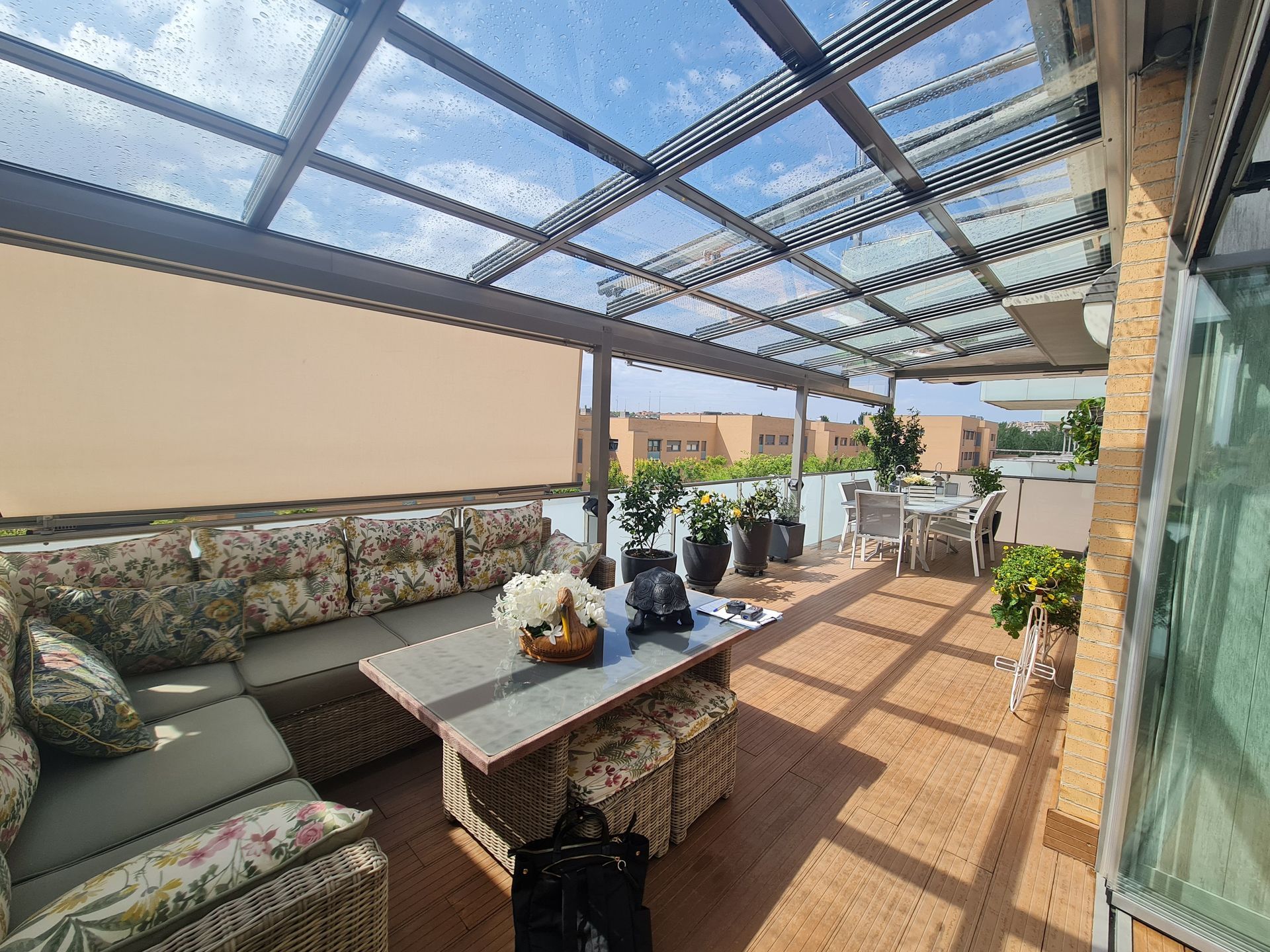 Un patio con sofá, mesa y sillas bajo un techo de cristal.