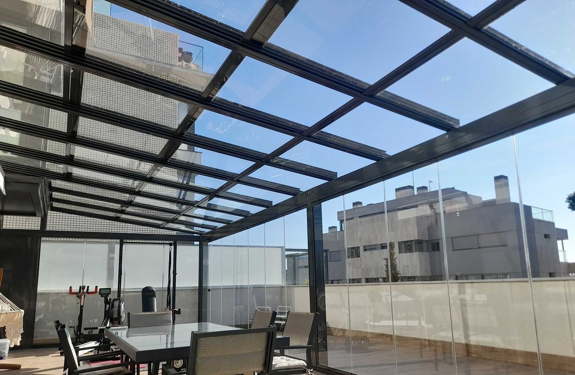 Un patio con mesa y sillas bajo un techo de cristal.