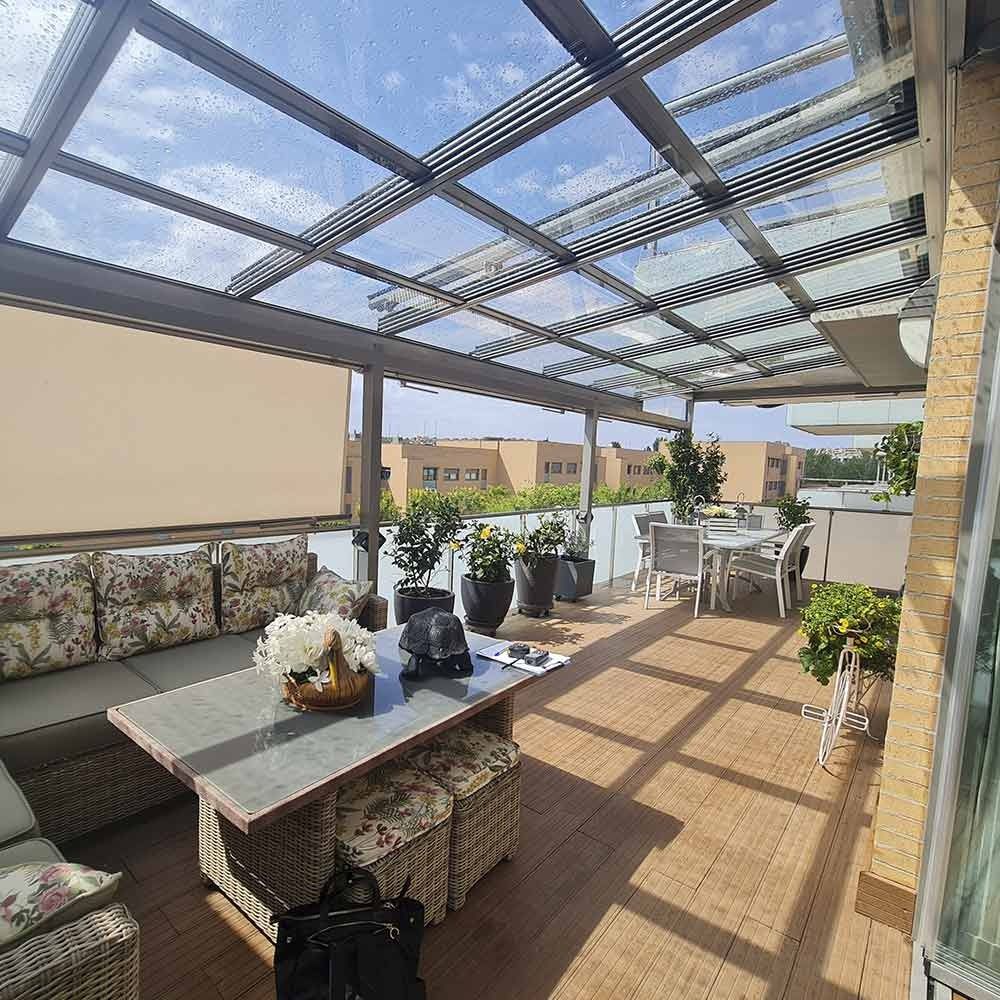 Un patio con mesa y sillas bajo un techo de cristal.