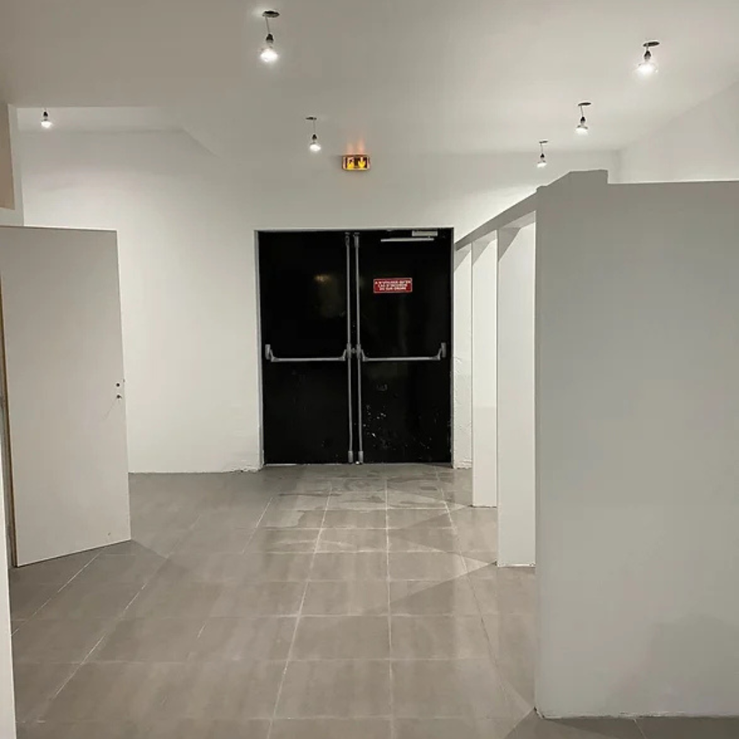 Un couloir avec une porte noire et un panneau de sortie rouge.