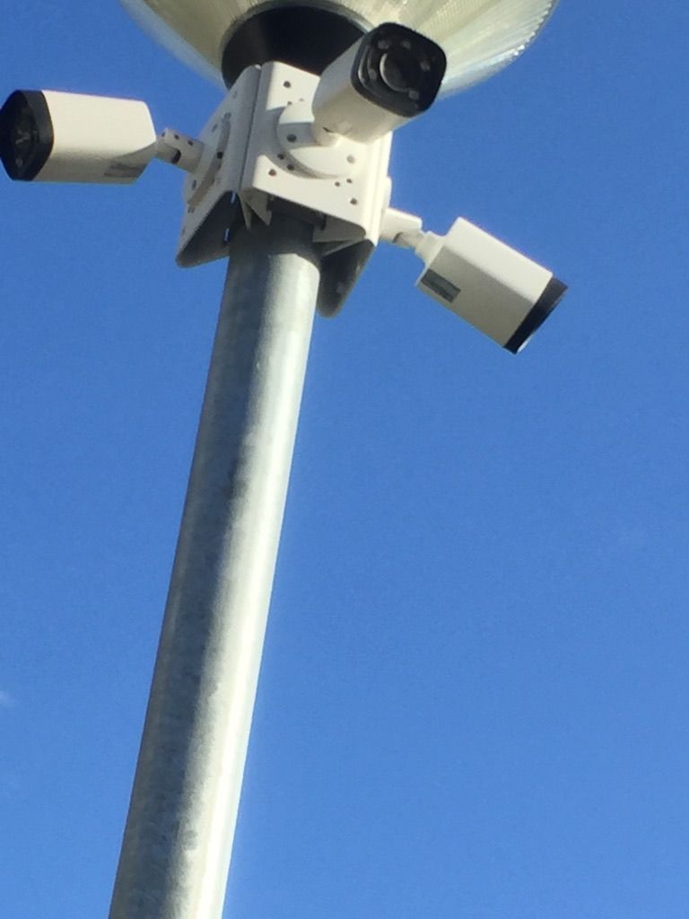 Caméras de sécurité montées sur un poteau métallique contre un ciel bleu.