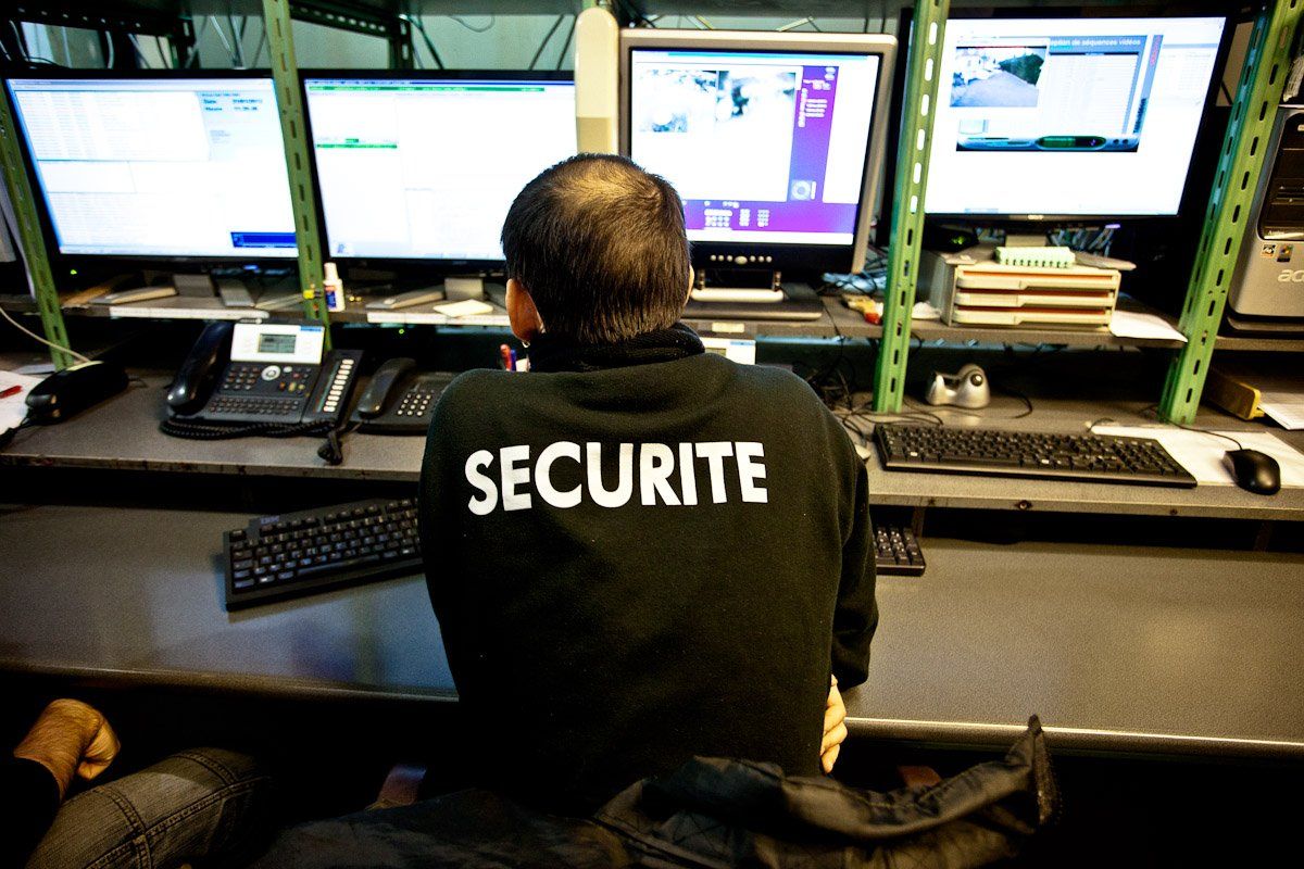 Une personne portant un t-shirt « SECURITE » surveille plusieurs écrans à un poste de sécurité.