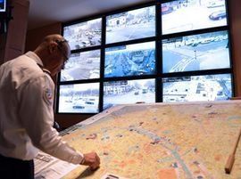 Un homme en uniforme surveille les écrans de vidéosurveillance et une carte dans une salle de contrôle.