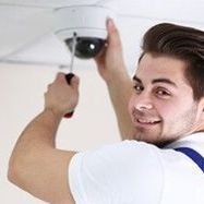 Un homme installe une caméra de sécurité au plafond, souriant.