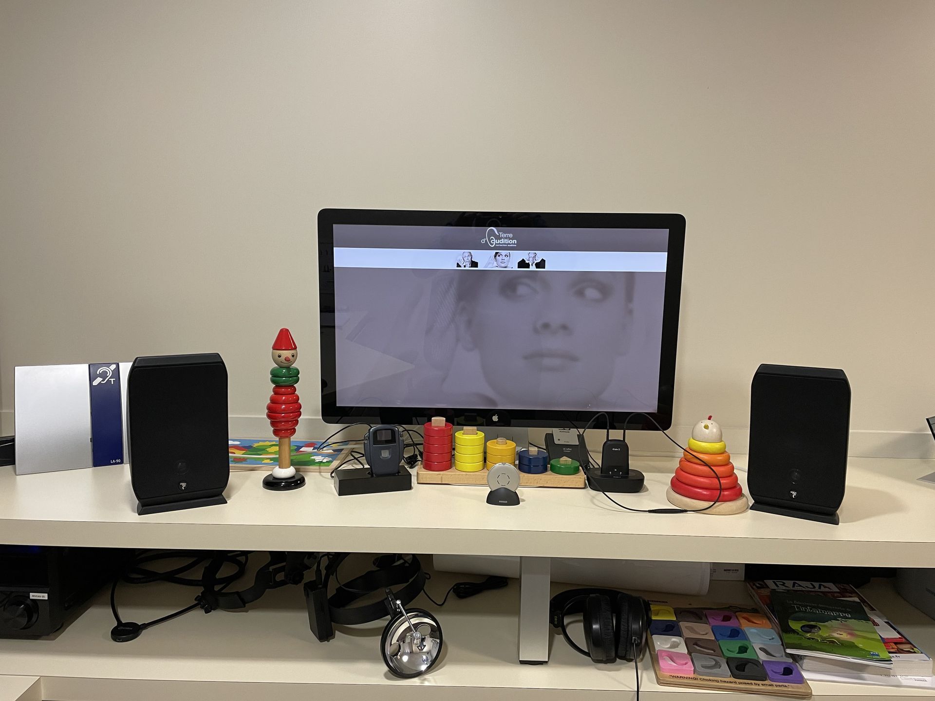 Bureau avec écran d'ordinateur, haut-parleurs et jouets colorés sur une étagère dans un bureau à domicile.