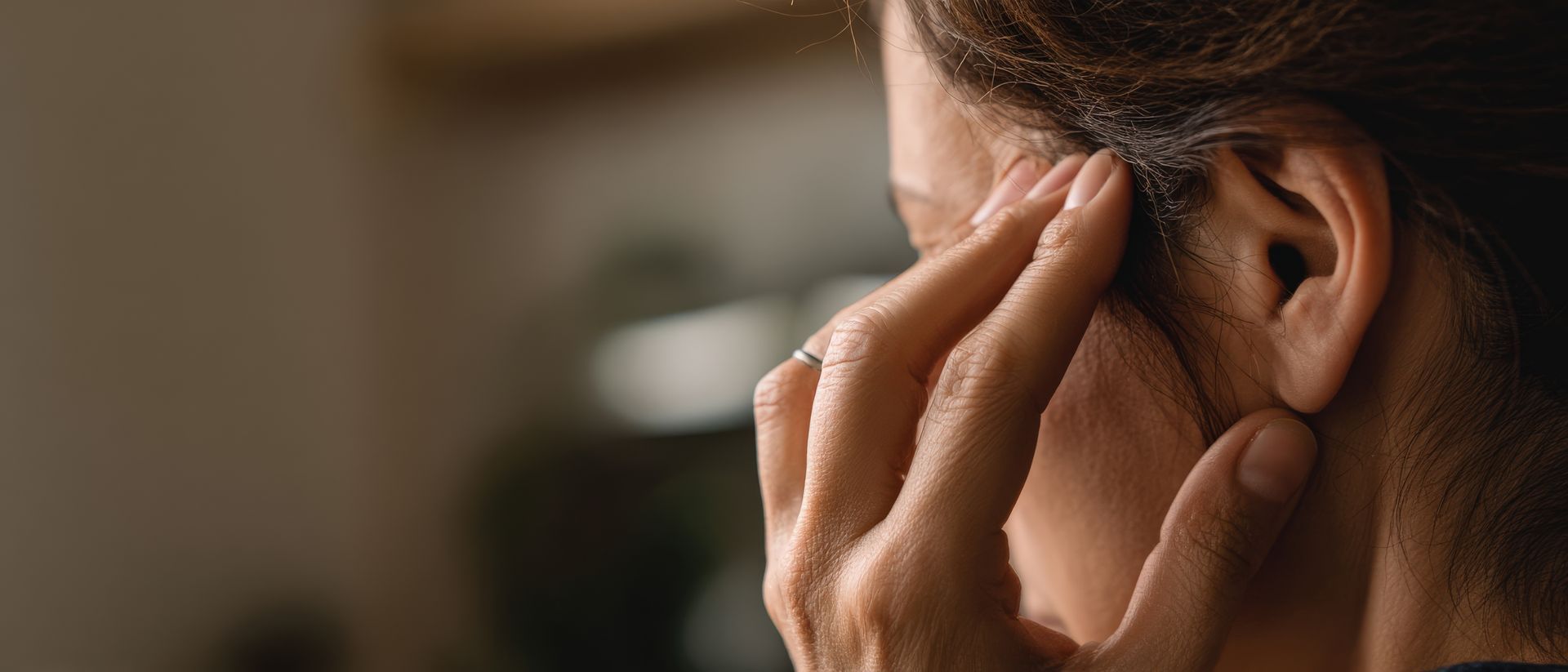 Gros plan sur une personne se tenant l'oreille, visiblement gênée, sur fond flou.
