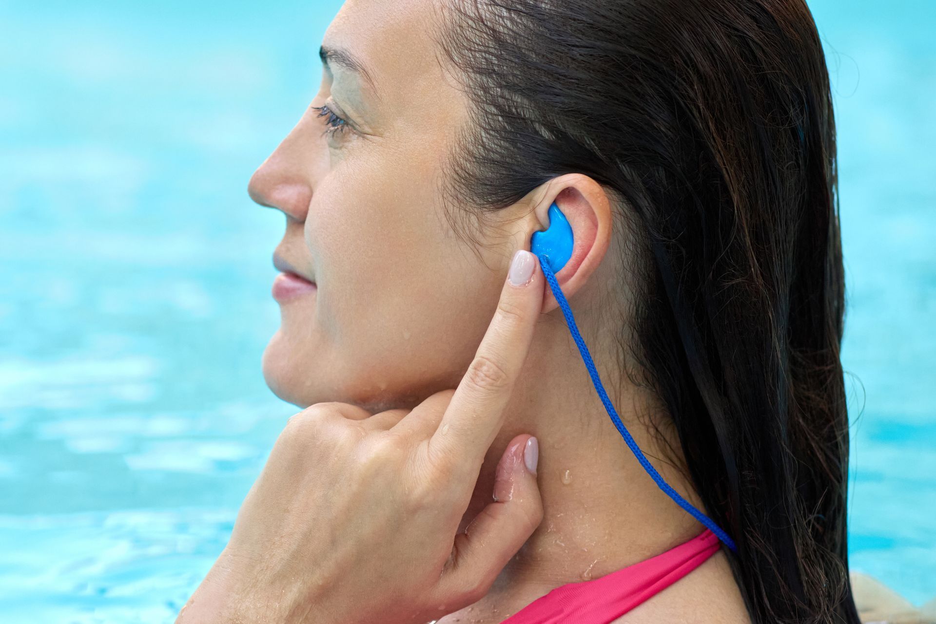 Une femme dans une piscine porte des bouchons d'oreille bleus et touche son oreille avec un cordon bleu attaché.