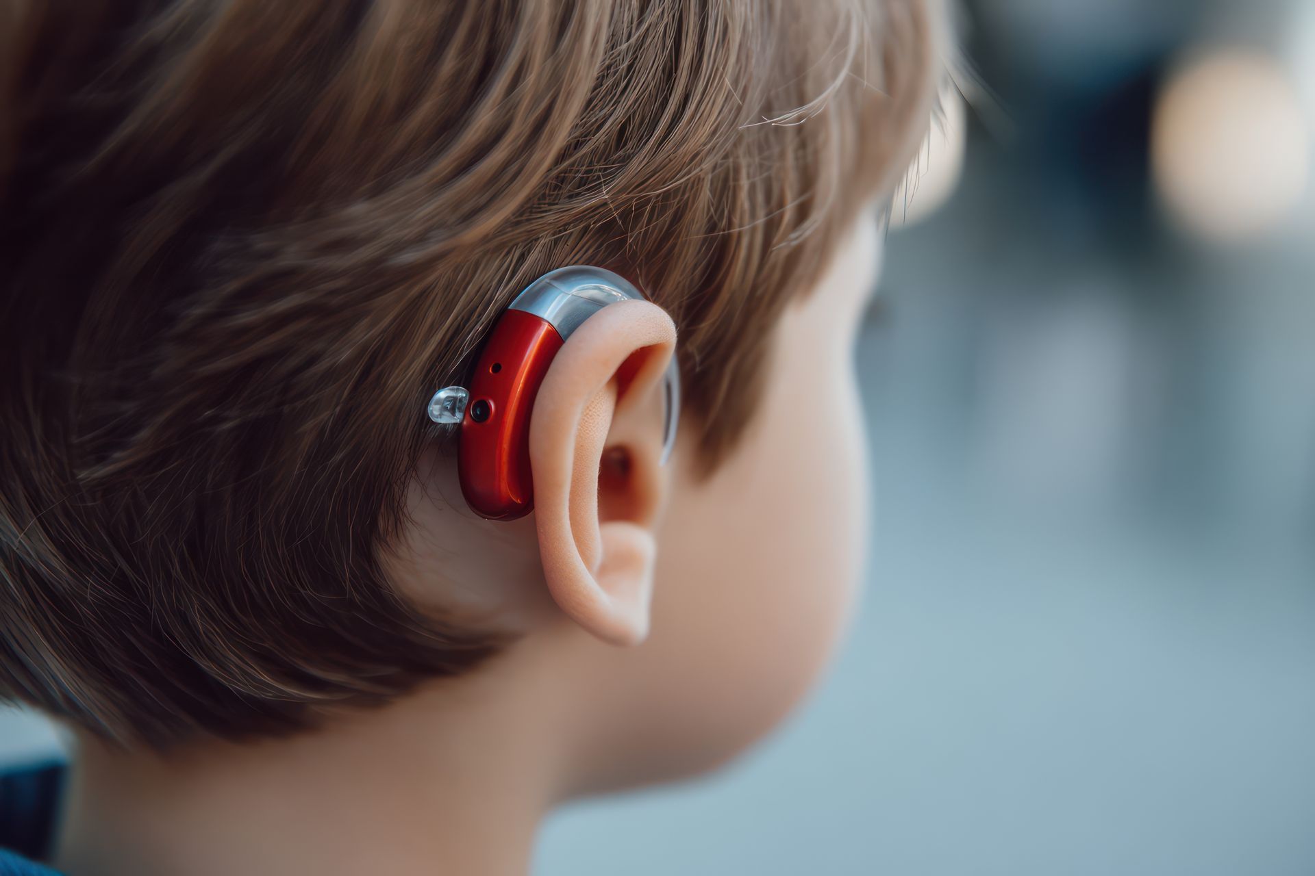Enfant portant un appareil auditif rouge derrière l'oreille, vu de profil à l'extérieur