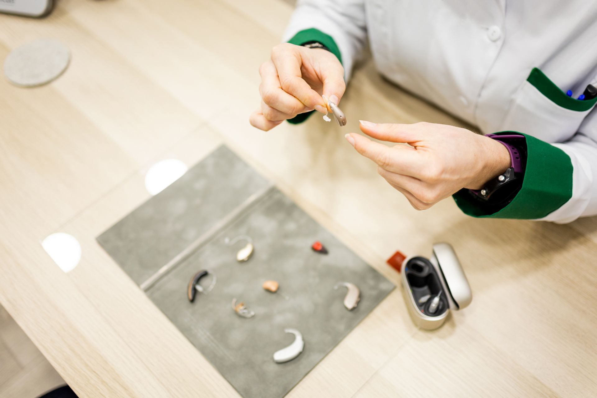 Des mains assemblent un petit appareil auditif sur un établi, à l'aide de pièces et d'outils.