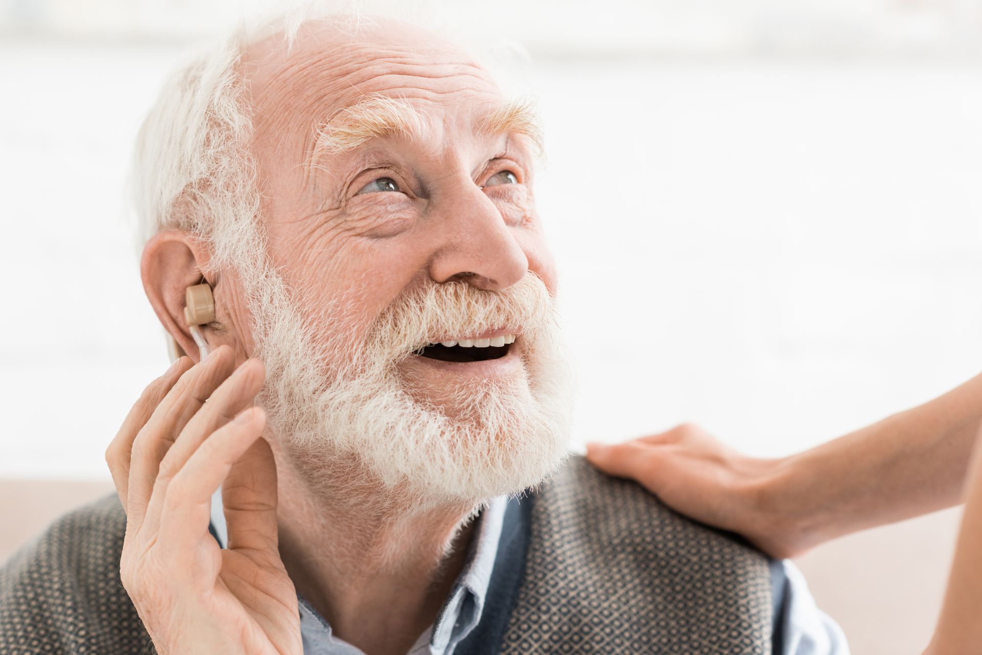 Un homme âgé souriant à la barbe blanche reçoit un massage des épaules dans une pièce lumineuse