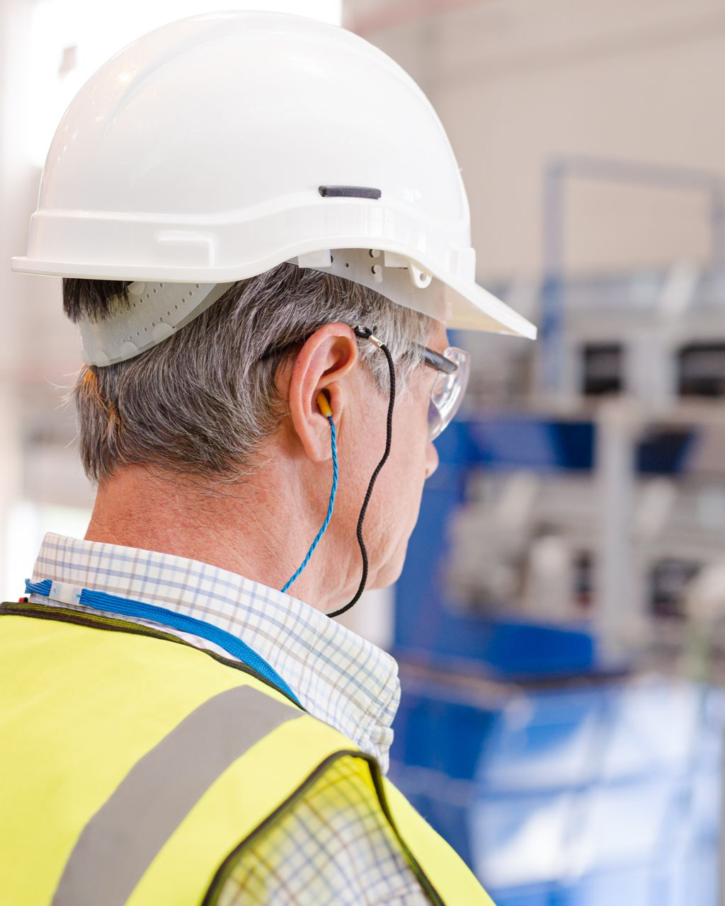 Ouvrier portant un casque blanc et un gilet réfléchissant avec protection auditive dans un environnement industriel