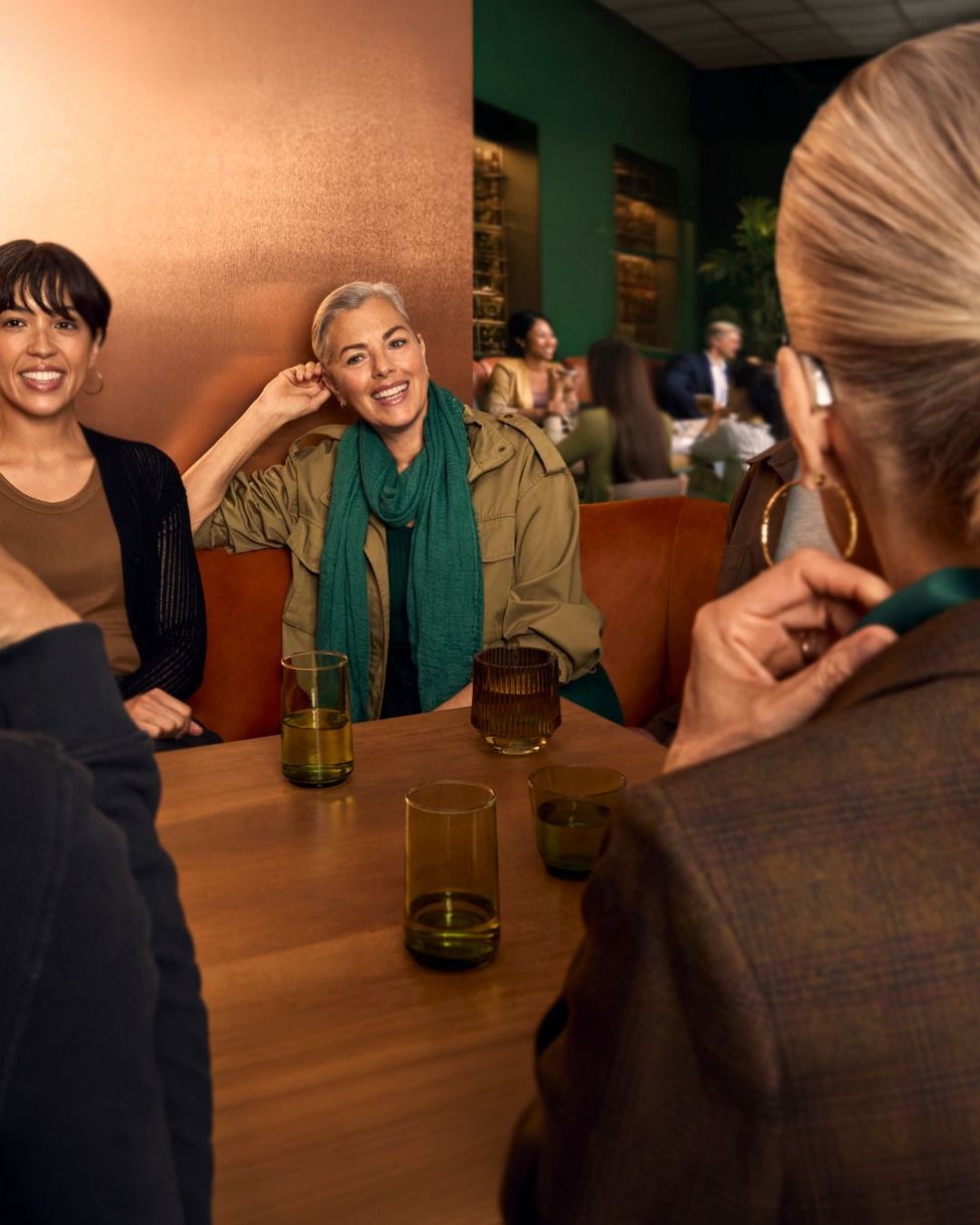 Des amis discutent autour d’une table dans un restaurant à l’éclairage chaleureux, avec des boissons et des visages souriants