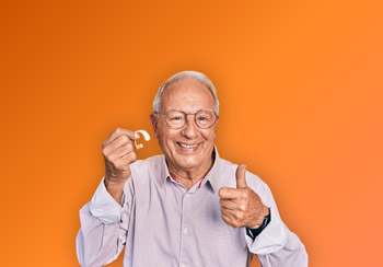 Un homme souriant portant des lunettes tient une clé et lève le pouce sur fond orange.