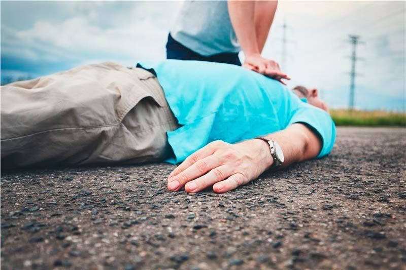 Un hombre yace en el suelo con una mujer dándole un masaje cardíaco.