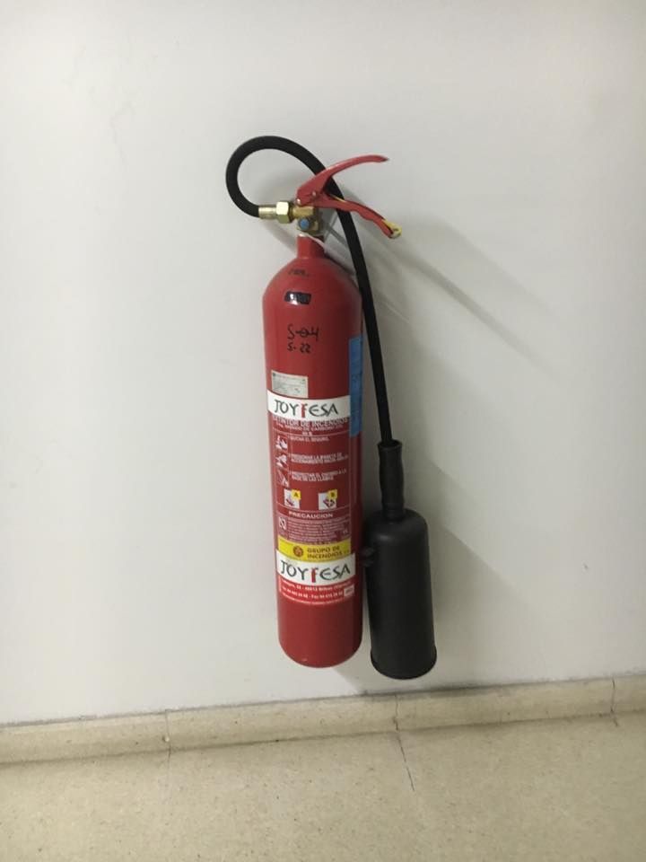 Un extintor rojo está colgado en una pared blanca.