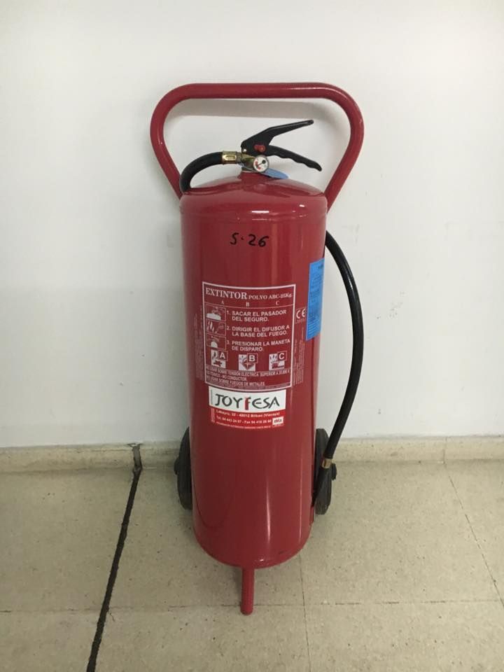 Un extintor rojo está en el suelo delante de una pared blanca.