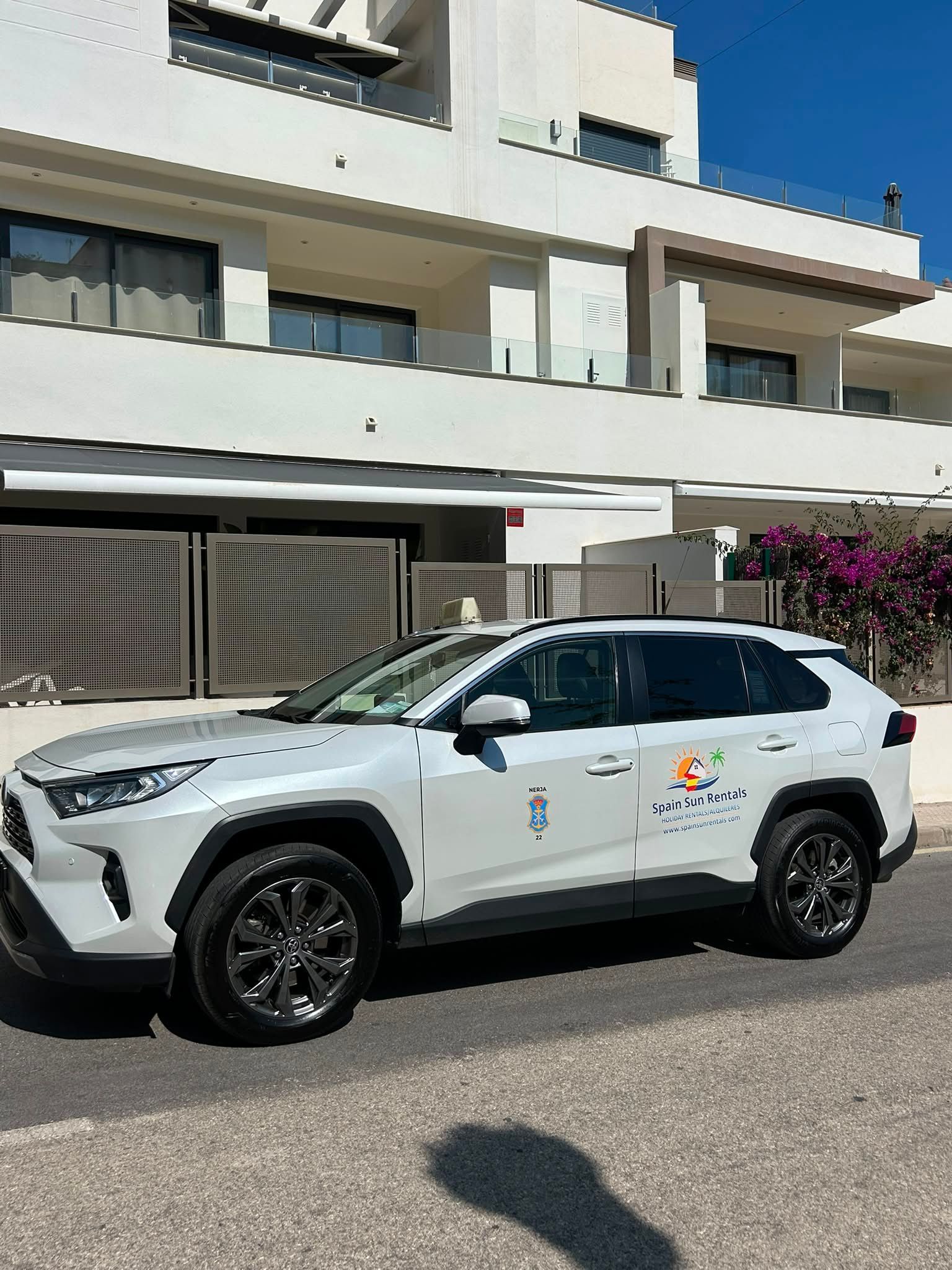 Una mujer mete una maleta en un coche blanco con el maletero abierto en una calle de la ciudad.