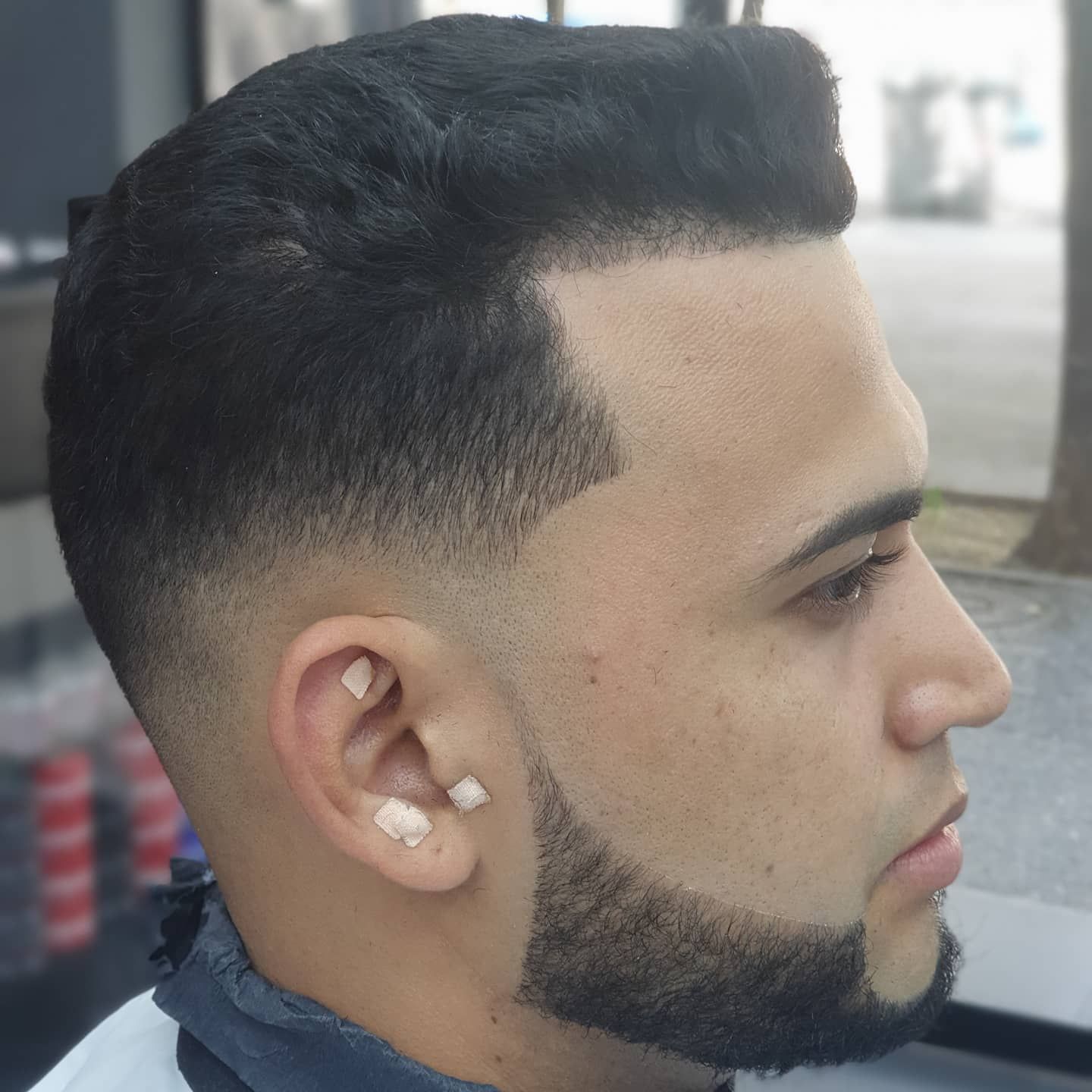 Hombre con corte de pelo y barba descoloridos. Tiene la línea del cabello recta y piel clara.