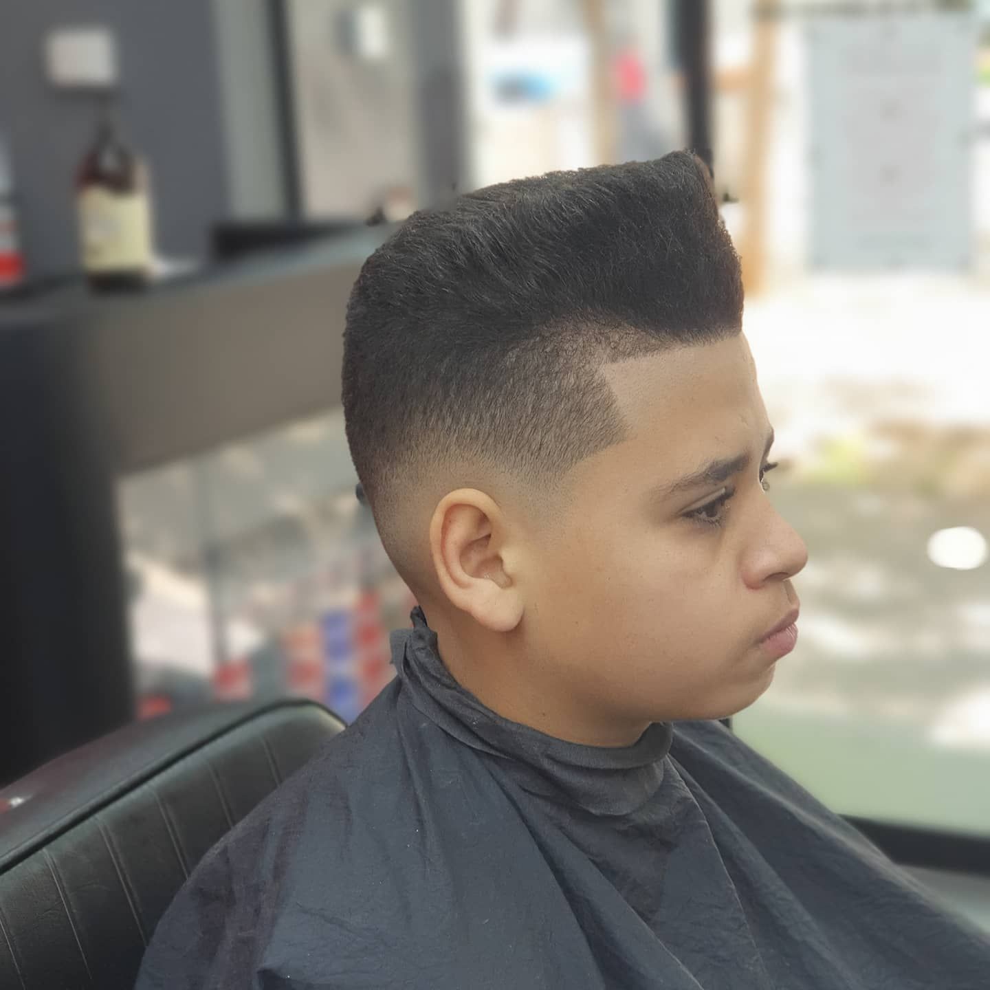 Niño con un peinado alto y degradado en una barbería, vista de perfil lateral.